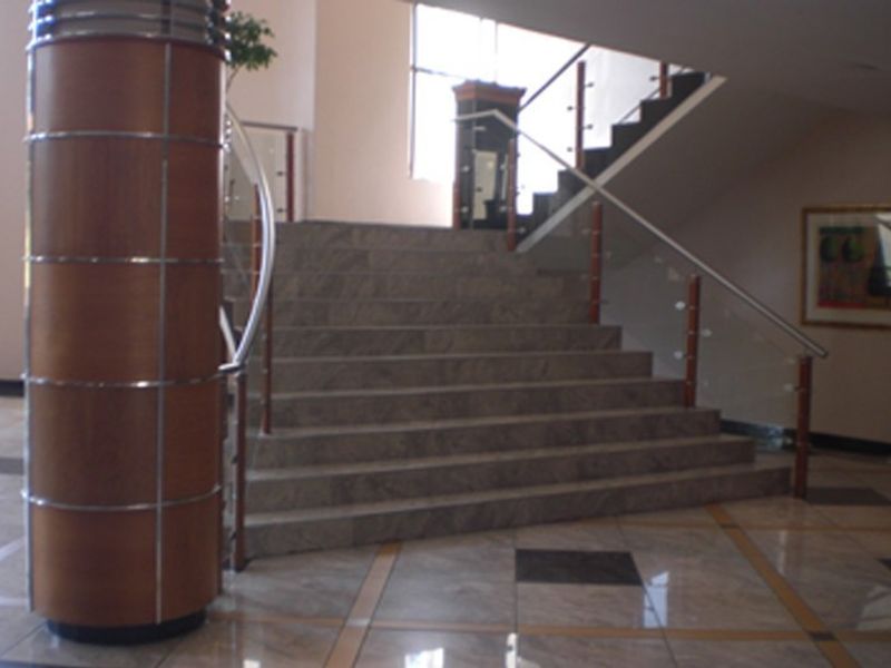 A grand commercial entrance foyer featuring polished stone flooring, a prominent decorative column, and a stone staircase with a modern glass and wood balustrade.