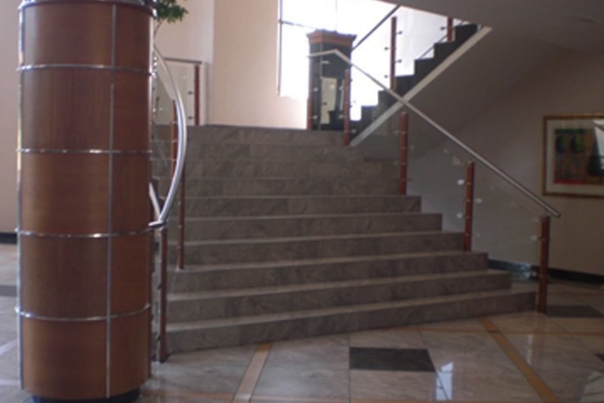 A grand commercial entrance foyer featuring polished stone flooring, a prominent decorative column, and a stone staircase with a modern glass and wood balustrade.