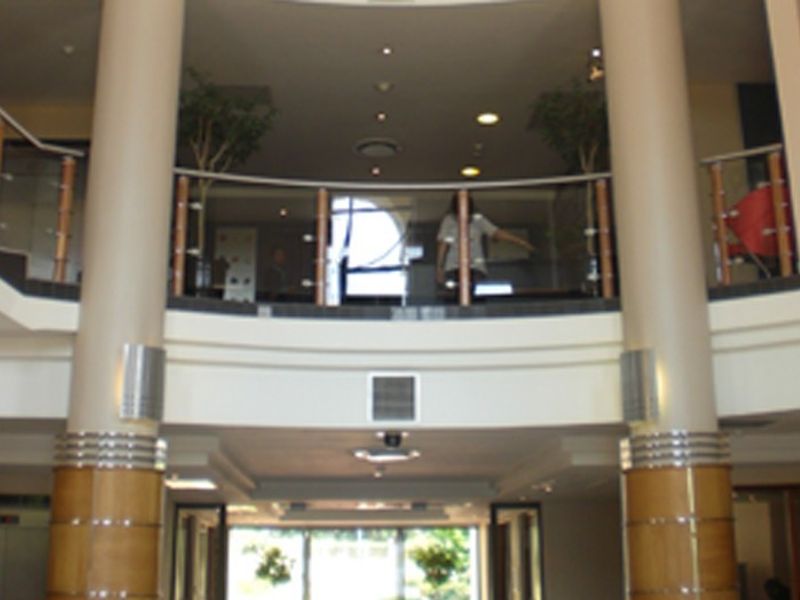 A grand commercial entrance foyer featuring prominent structural columns, a curved mezzanine level with glass balustrading, and integrated architectural lighting.