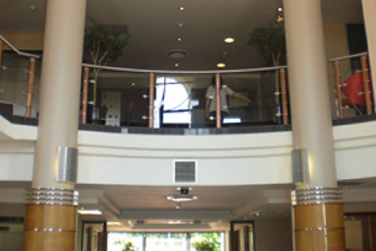 A grand commercial entrance foyer featuring prominent structural columns, a curved mezzanine level with glass balustrading, and integrated architectural lighting.
