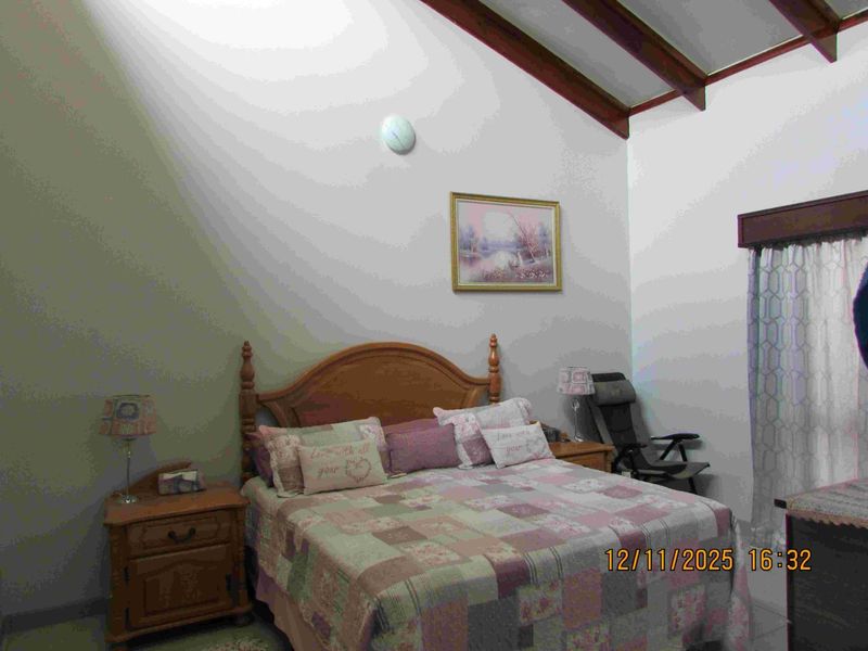 A bedroom featuring a vaulted ceiling with exposed timber beams, providing a spacious feel with natural light through the window.
