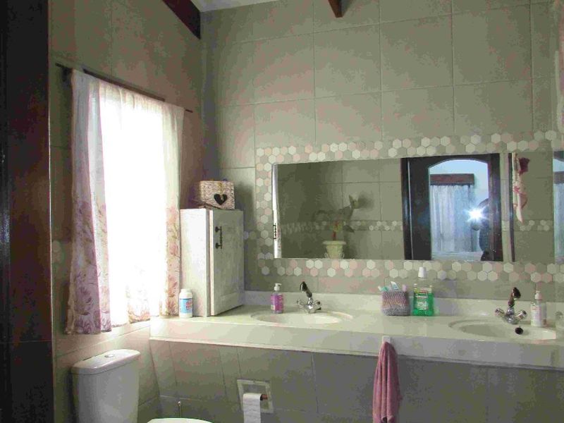 A functional bathroom featuring a double vanity, tiled walls, and exposed ceiling beams, offering a dated aesthetic ready for modernization.