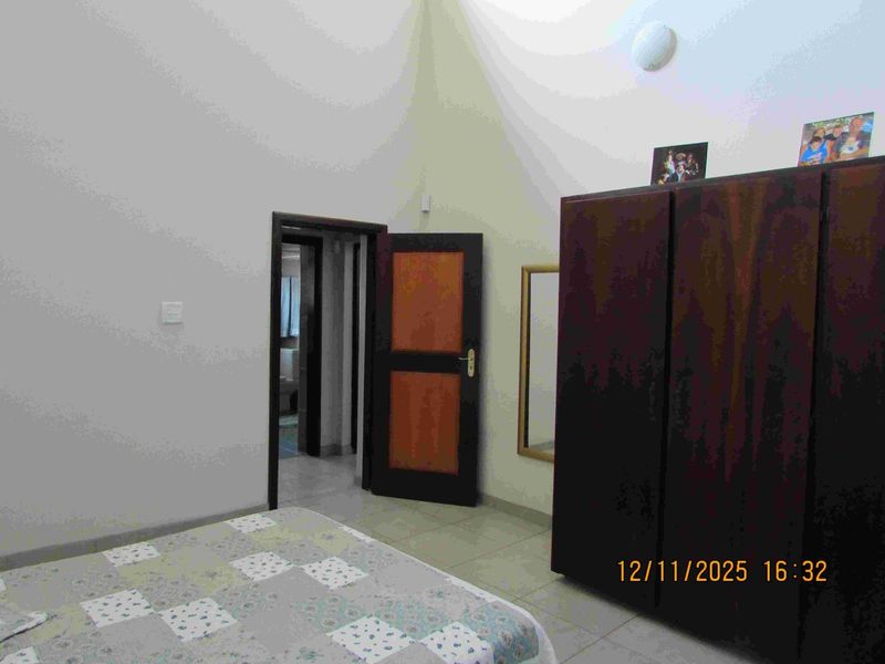 A bedroom featuring tiled flooring and a vaulted ceiling, providing a functional space with direct access to an adjoining room.