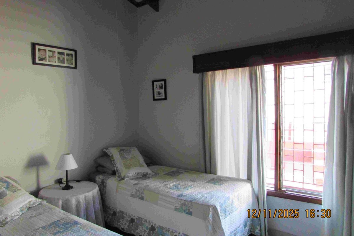 A bedroom featuring exposed timber ceiling beams and a window fitted with security bars, providing natural light.