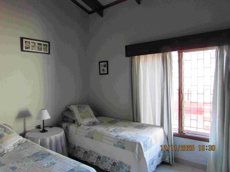 A bedroom featuring exposed timber ceiling beams and a window fitted with security bars, providing natural light.