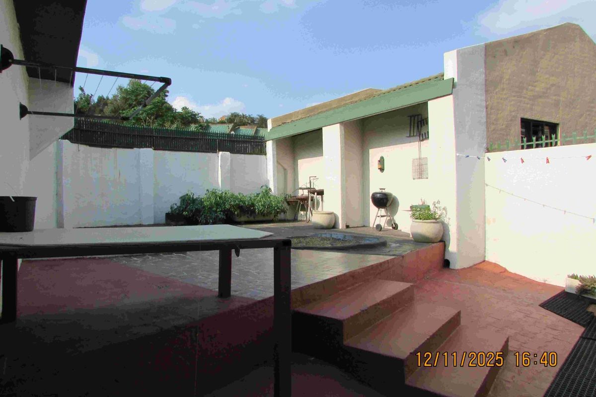 A rear courtyard area featuring a raised patio, built-in braai, and perimeter walling, offering a functional outdoor space in need of cosmetic maintenance.