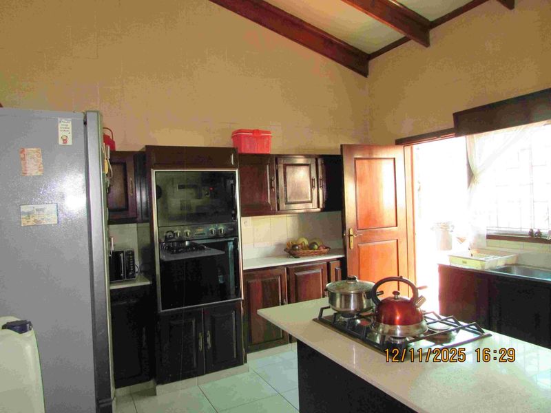 A functional kitchen featuring dark wood cabinetry, a built-in oven, gas hob, and tiled flooring with exposed timber ceiling beams.