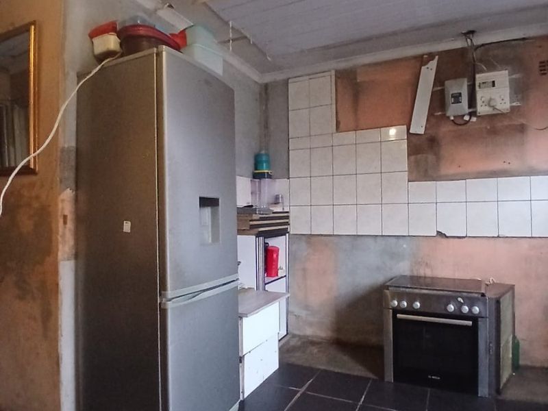 A kitchen area in need of significant renovation, featuring tiled flooring, a built-in oven, and unfinished wall surfaces with exposed electrical components.