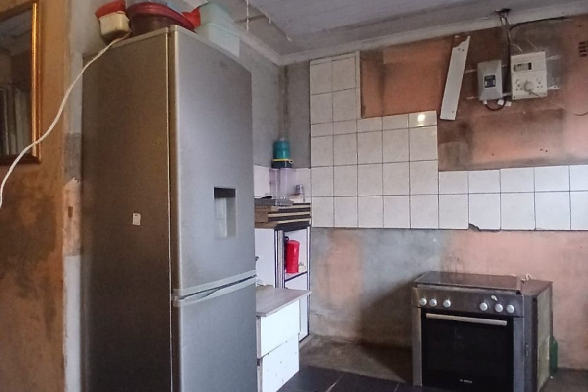 A kitchen area in need of significant renovation, featuring tiled flooring, a built-in oven, and unfinished wall surfaces with exposed electrical components.