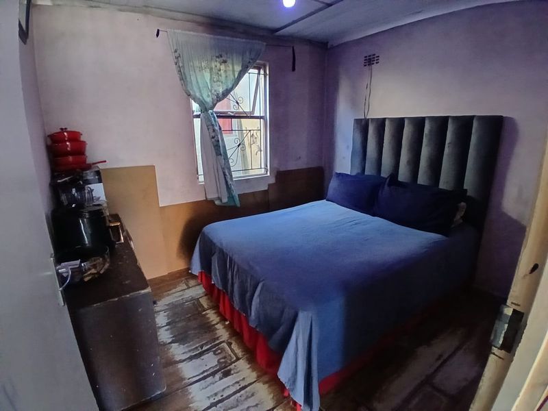 A bedroom featuring a window with security bars and worn flooring, requiring cosmetic updates to improve the overall condition and appeal.