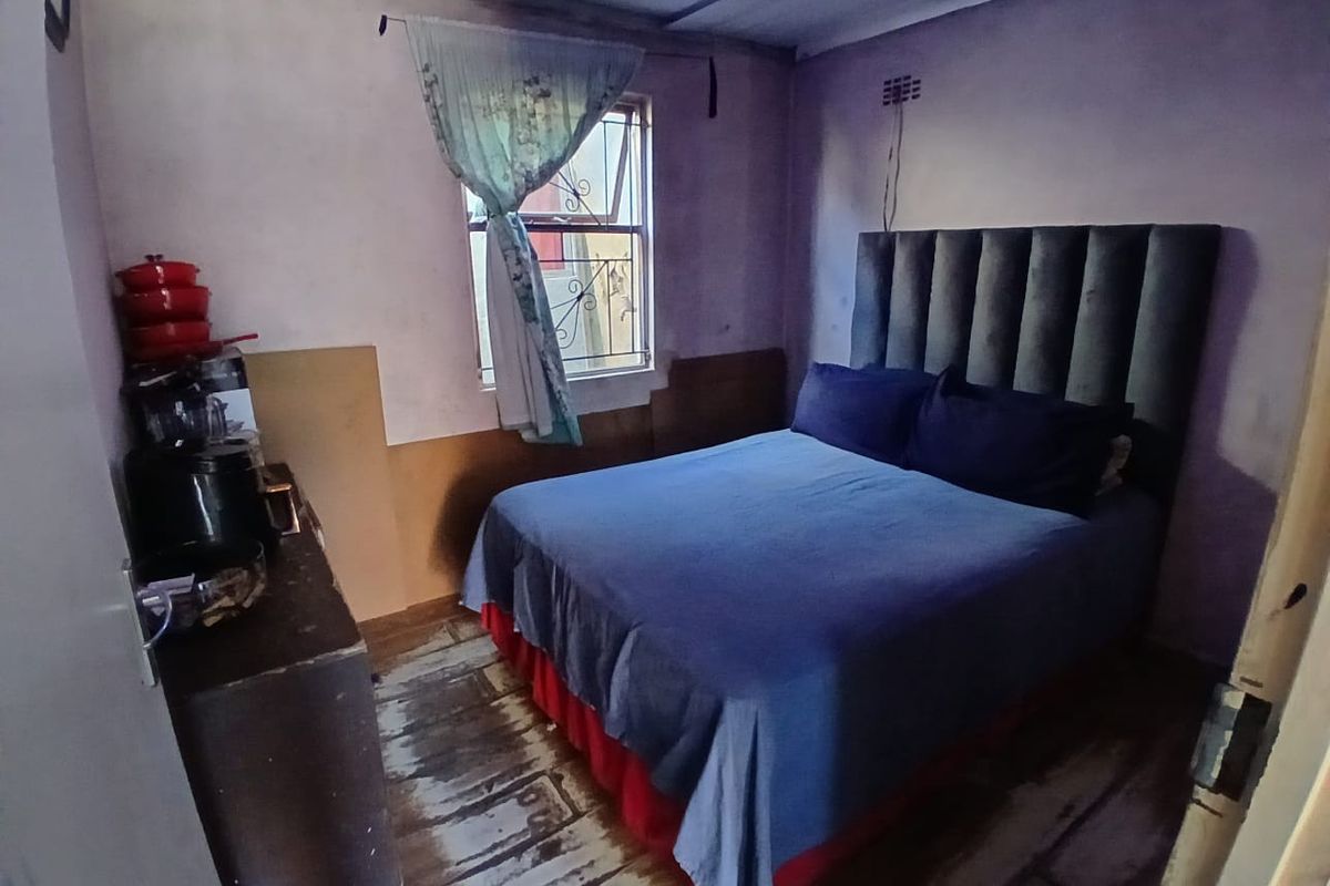 A bedroom featuring a window with security bars and worn flooring, requiring cosmetic updates to improve the overall condition and appeal.
