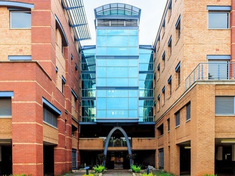 Front elevation of a modern commercial office building featuring a prominent glass atrium, brick facade, and integrated ground-level covered parking.