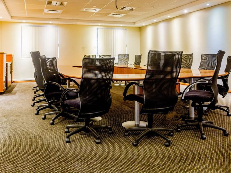 A professional boardroom featuring a large meeting table, recessed ceiling lighting, and carpeted flooring, suitable for corporate meetings and collaborative work sessions.