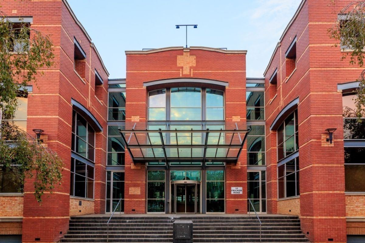 Professional front elevation of a commercial office building featuring a prominent brick facade, glass entrance canopy, and wide concrete staircase.