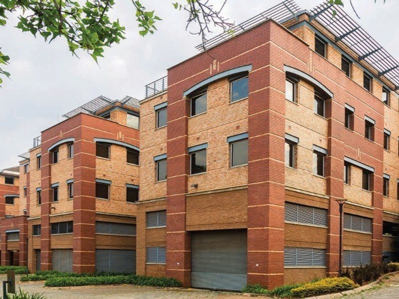 A multi-story commercial building featuring a face brick facade, roller shutter access points, and integrated louvred window shutters with a paved exterior approach.