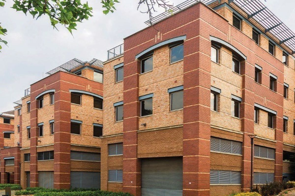 A multi-story commercial building featuring a face brick facade, roller shutter access points, and integrated louvred window shutters with a paved exterior approach.