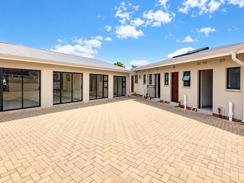 A spacious paved rear courtyard featuring modern sliding glass doors, clean exterior finishes, and functional drainage and utility infrastructure.