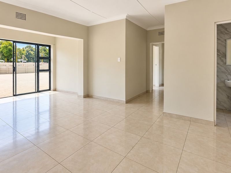 Spacious, light-filled living area featuring neutral tiled flooring, large sliding glass doors, and an adjacent bathroom with a modern pedestal basin.