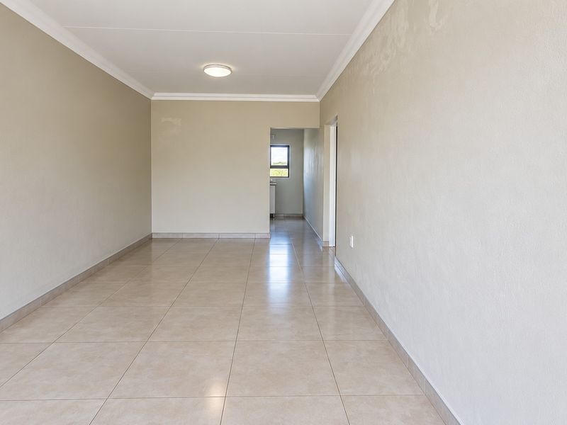 An empty, neutral-toned living area featuring tiled flooring, coved ceilings, and a clean, minimalist layout ready for personalization.
