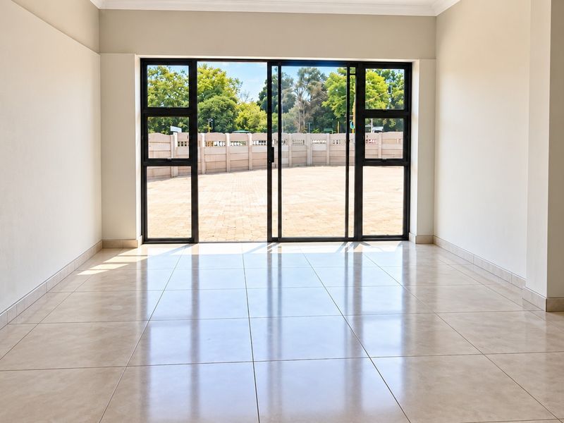 A bright, empty living room featuring neutral tiled flooring and large sliding glass doors that open to an outdoor paved area.