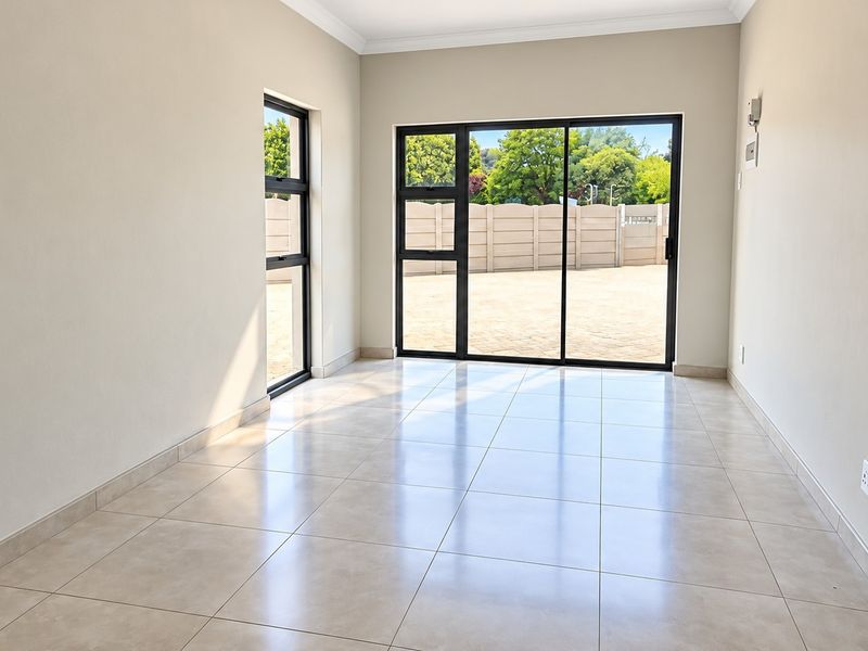A bright, empty living area featuring neutral tiled flooring, modern aluminium sliding doors, and large windows providing ample natural light.