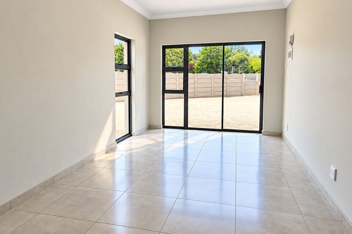 A bright, empty living area featuring neutral tiled flooring, modern aluminium sliding doors, and large windows providing ample natural light.