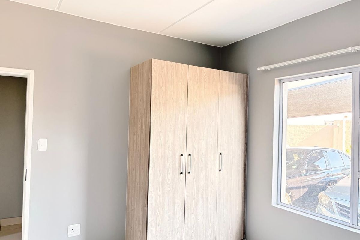 A clean, neutral-toned bedroom featuring a modern built-in wardrobe and a large window providing natural light.
