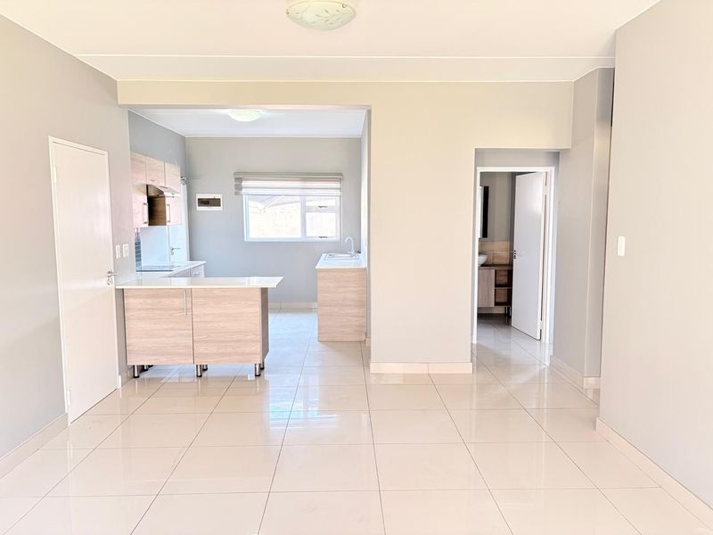 Bright open-plan living area featuring modern tiled flooring, a functional kitchen with built-in cabinetry, and access to an adjoining bathroom.