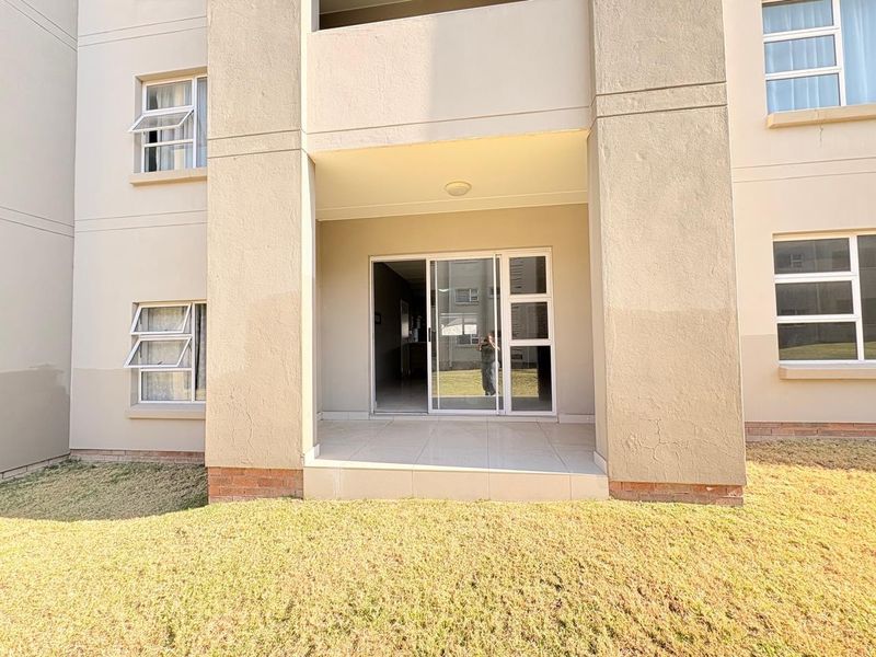 A ground floor patio area featuring tiled flooring and a sliding glass door entrance, set against the exterior facade of the apartment building.