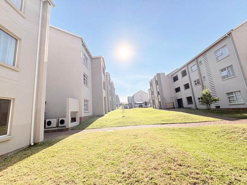 A view of the apartment complex exterior featuring a well-maintained lawn, paved pathways, and modern building facades.