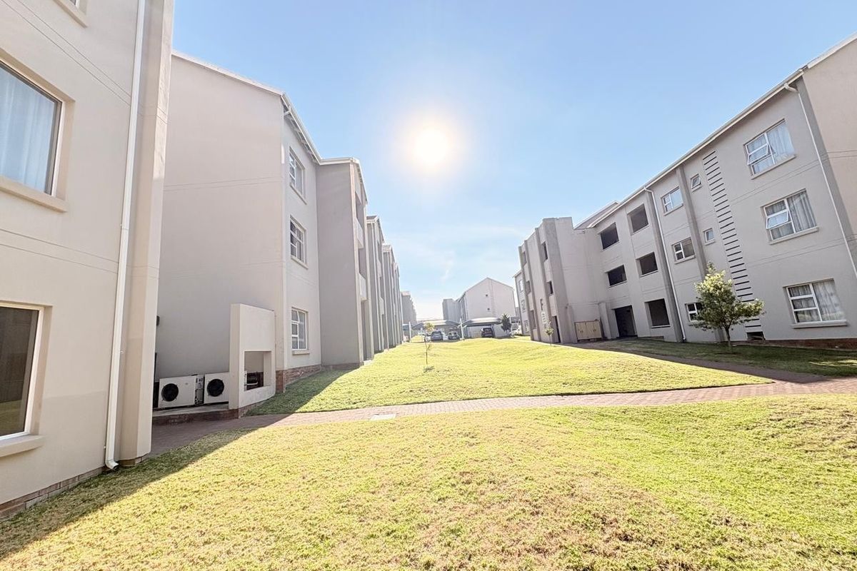 A view of the apartment complex exterior featuring a well-maintained lawn, paved pathways, and modern building facades.