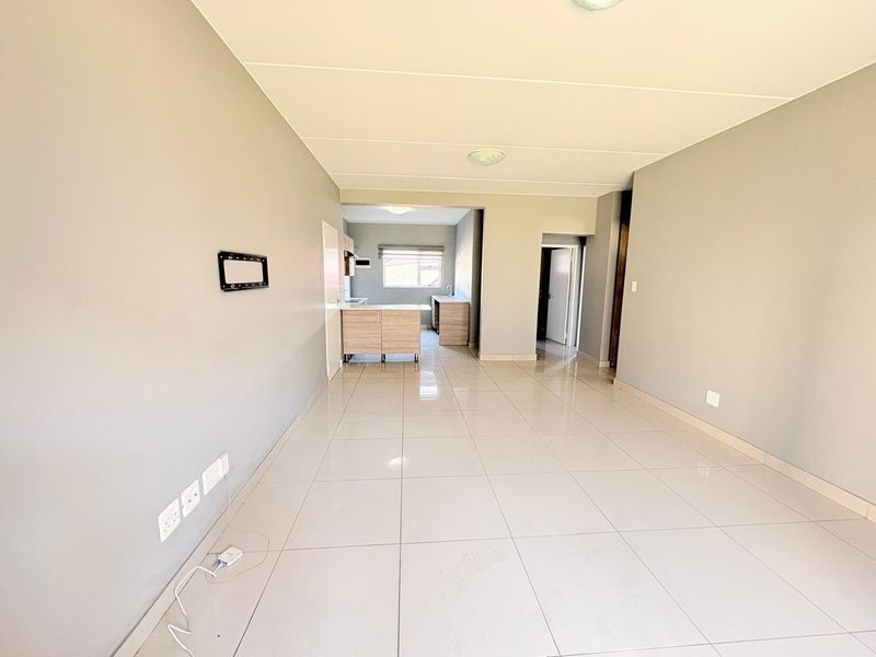 Spacious open-plan living area featuring neutral tiled flooring and a functional kitchen with built-in cabinetry, offering a clean and versatile layout.