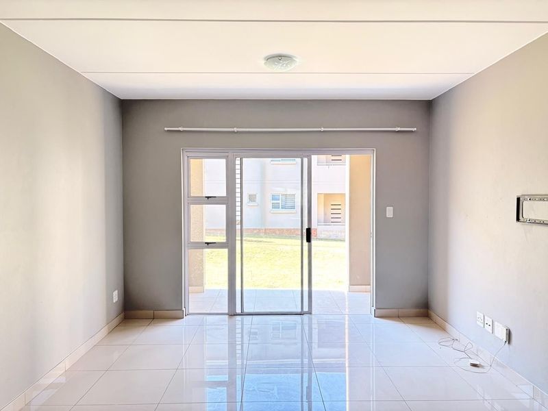 A bright, empty living room featuring polished tile flooring, neutral grey walls, and a sliding glass door providing access to an outdoor patio area.