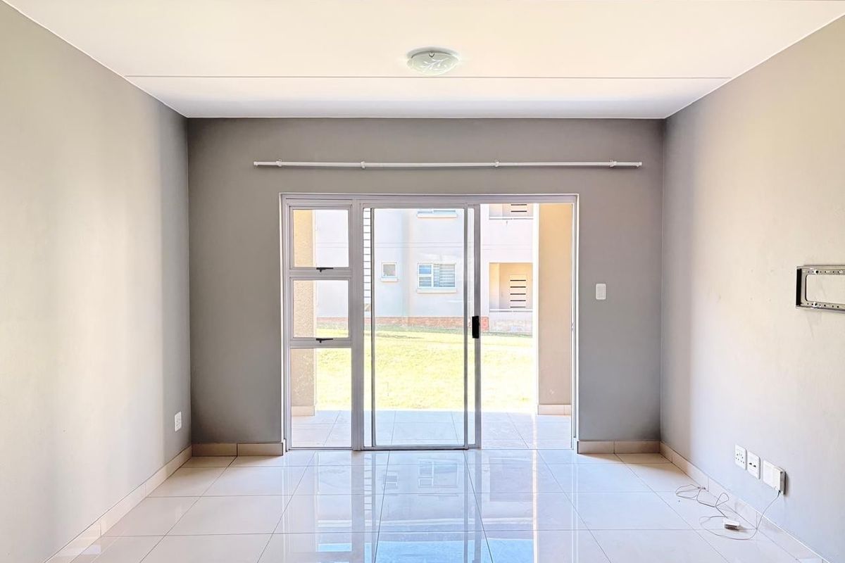 A bright, empty living room featuring polished tile flooring, neutral grey walls, and a sliding glass door providing access to an outdoor patio area.