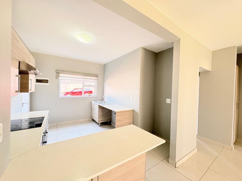 A clean, modern kitchen featuring light wood-finish cabinetry, a built-in electric hob with extractor, and a functional breakfast counter with tiled flooring.