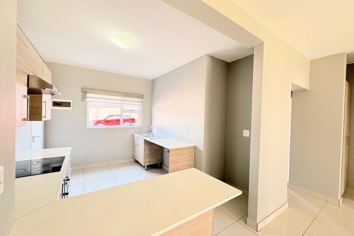 A clean, modern kitchen featuring light wood-finish cabinetry, a built-in electric hob with extractor, and a functional breakfast counter with tiled flooring.