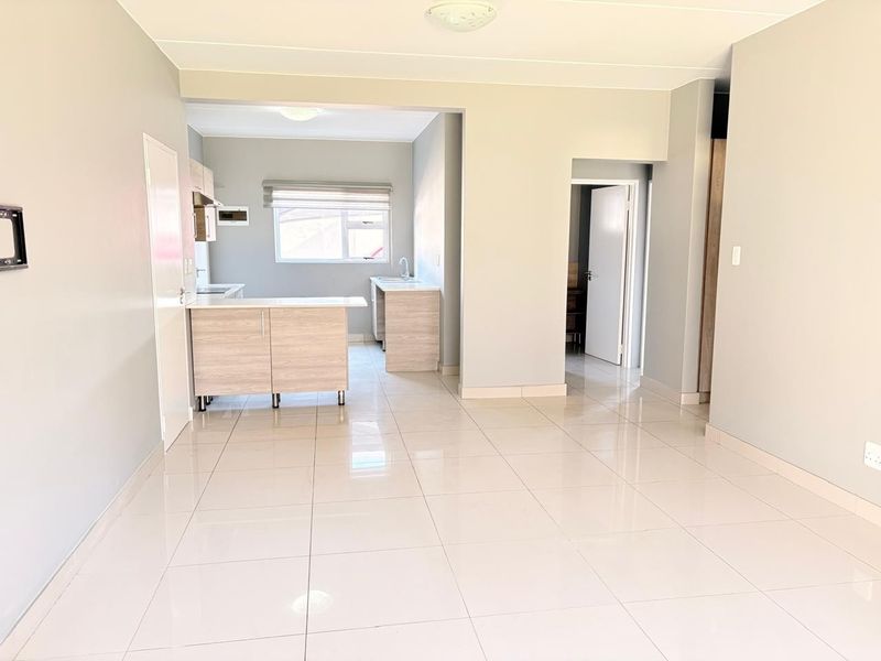 Spacious open-plan living area featuring neutral tiled flooring and a modern kitchen with built-in cabinetry and integrated fixtures.