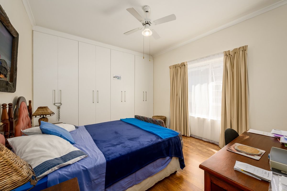 A well-maintained bedroom featuring extensive floor-to-ceiling built-in cupboards, a ceiling fan, and warm laminate flooring, offering a functional and comfortable living space.
