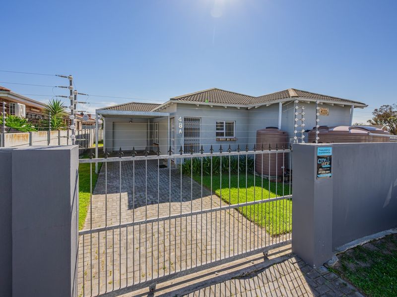 Front view of a single-story house featuring a paved driveway, secure metal gate, electric fencing, and external water storage tanks.