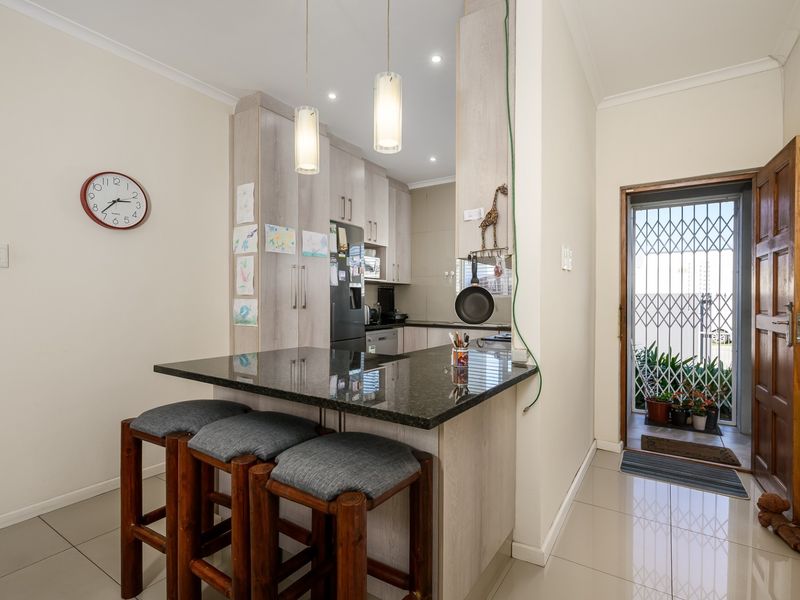 Compact kitchen featuring granite countertops, a breakfast bar, and built-in cabinetry, with direct access to an exterior entrance via a security gate.