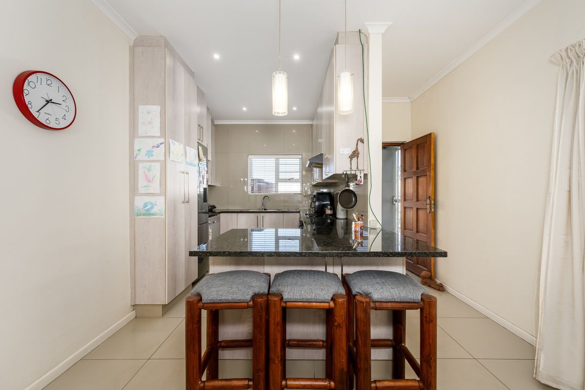 A functional kitchen featuring granite countertops, ample built-in cabinetry, and a breakfast bar area with pendant lighting, finished with neutral tiled flooring.