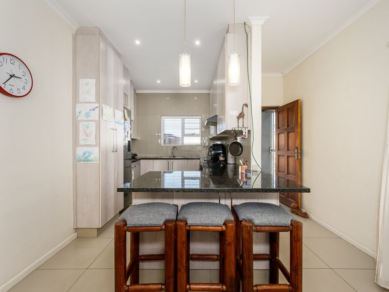 A functional kitchen featuring granite countertops, ample built-in cabinetry, and a breakfast bar area with pendant lighting, finished with neutral tiled flooring.