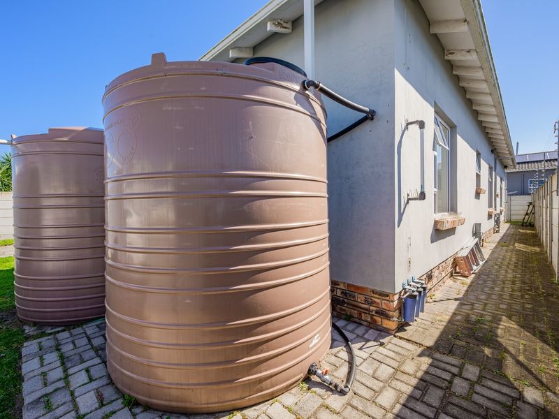 Side exterior view of the property featuring large water storage tanks, a paved walkway, and an integrated water filtration system.
