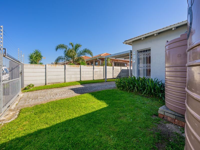 Front exterior view featuring a paved driveway, carport, water storage tank, and secure boundary wall with electric fencing.
