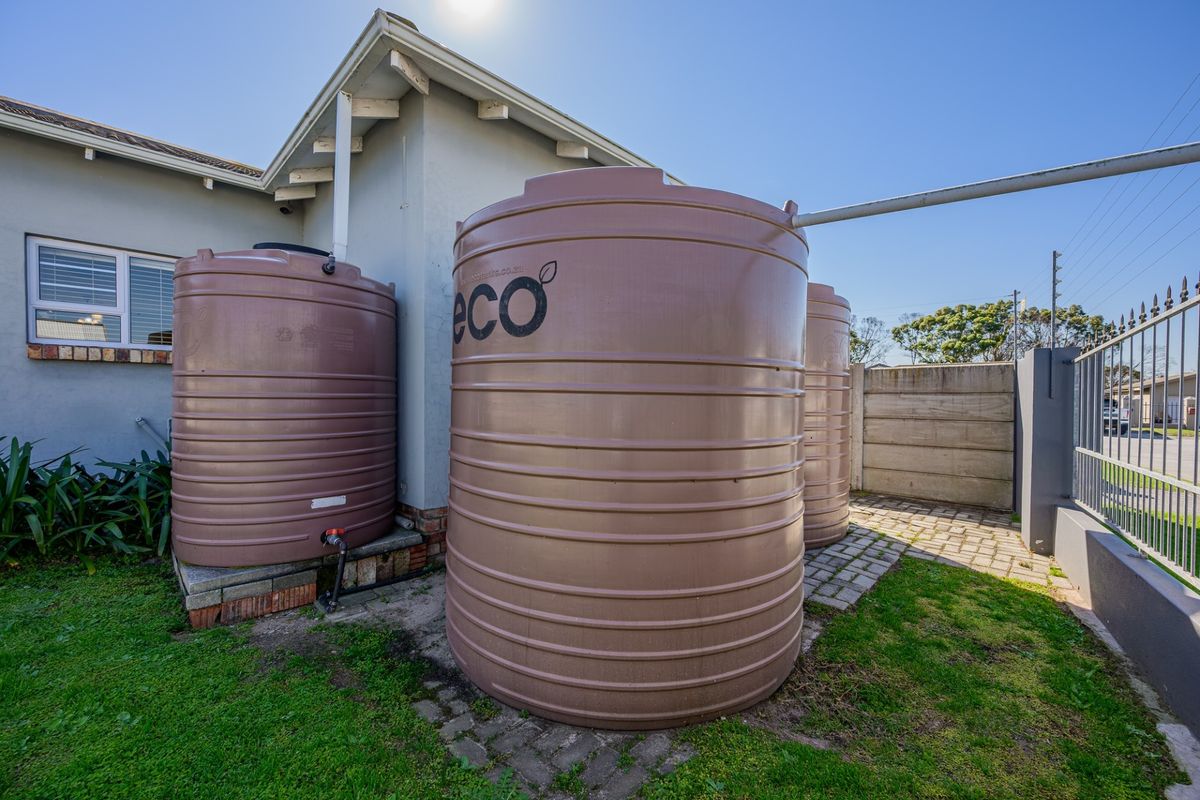 Exterior view of the property featuring multiple large water storage tanks installed on a paved area alongside the house structure.