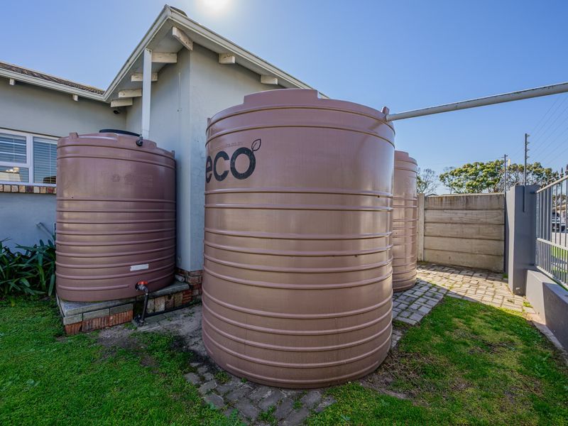 Exterior view of the property featuring multiple large water storage tanks installed on a paved area alongside the house structure.