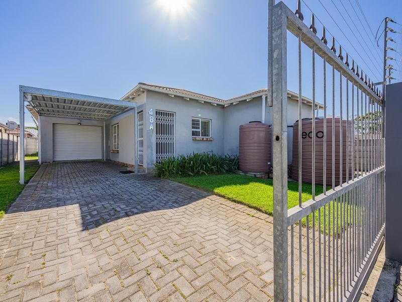 Front exterior view featuring a paved driveway, carport, garage, and secure perimeter fencing with installed water storage tanks.