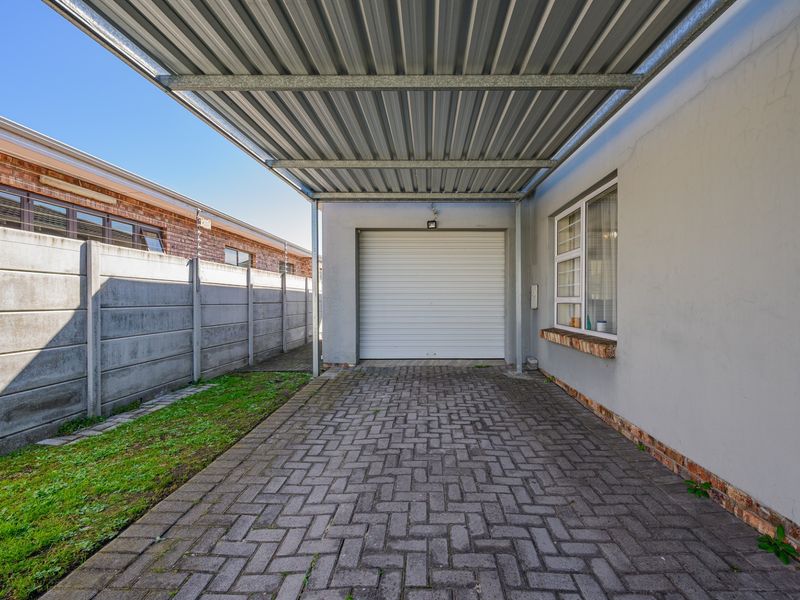 A covered carport area featuring a roller shutter garage door, paved driveway, and precast concrete boundary wall.