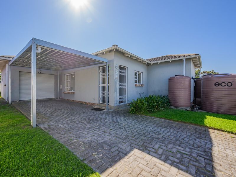 Front elevation of the house featuring a paved driveway, attached carport, garage, and external water storage tanks.