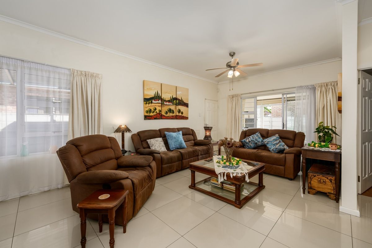 A bright and spacious living room featuring neutral tiled flooring, a ceiling fan, and large sliding glass doors providing access to the outdoor area.